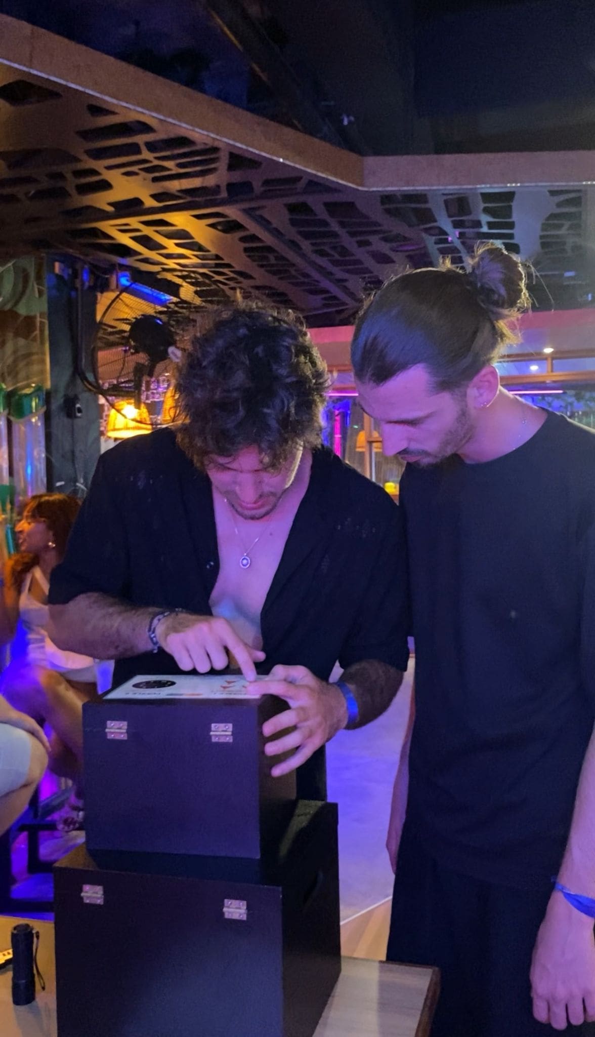 Two men examining a box in dimly lit room.