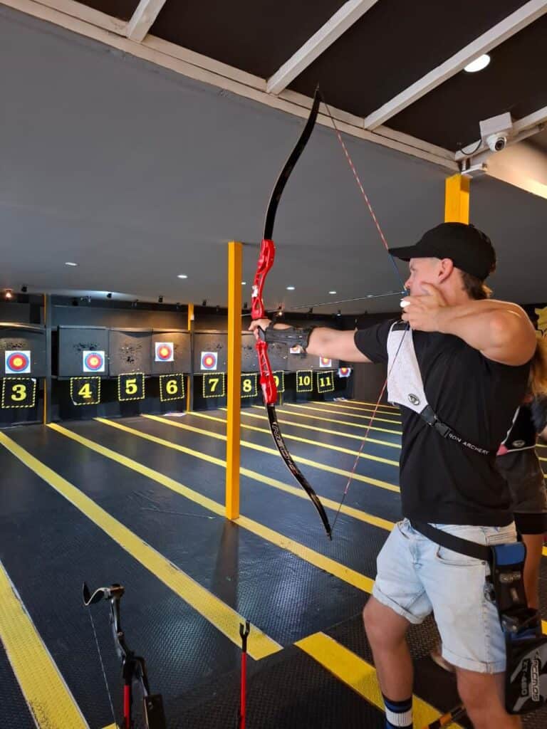 Man aiming bow at indoor archery range targets.